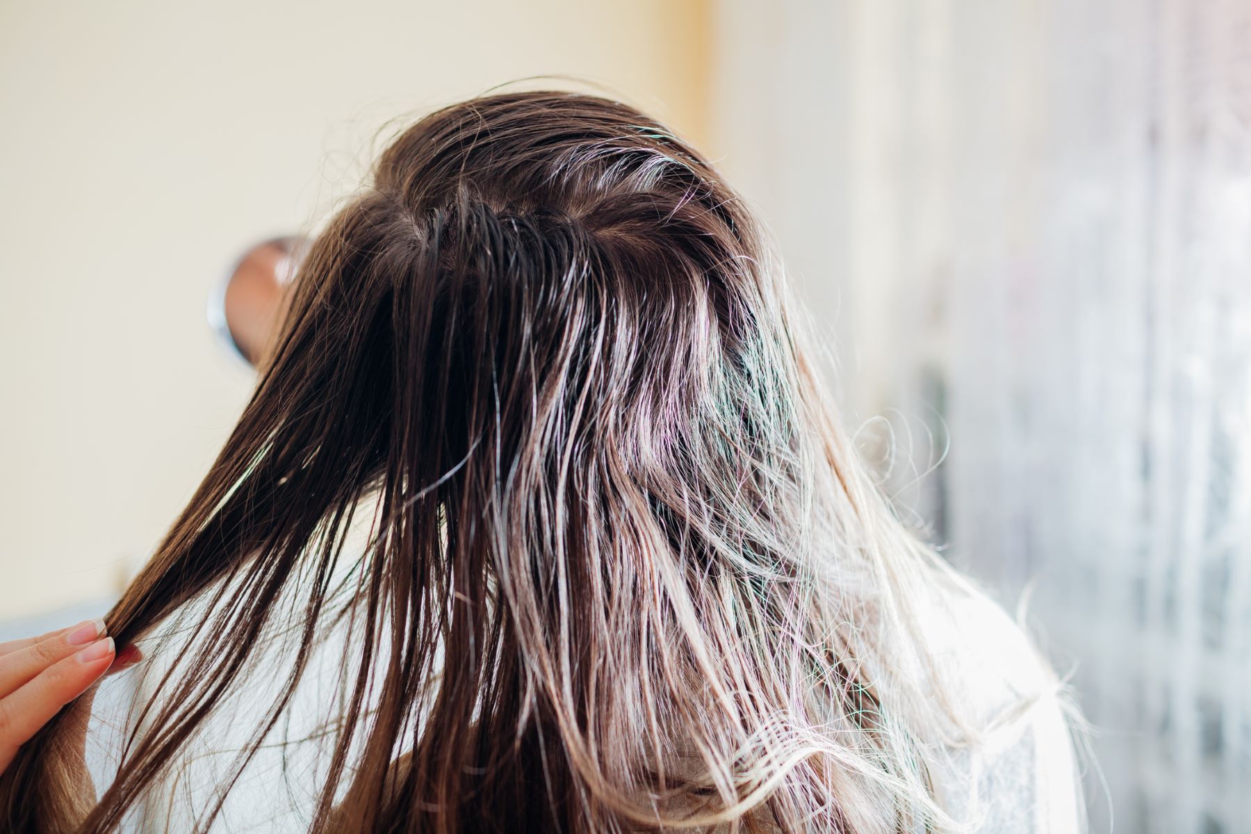 Woman inspects oily hair in the mirror